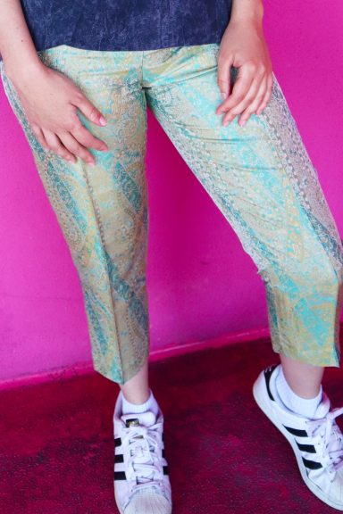 Person wearing snake-print cropped pants and white sneakers against a pink background.